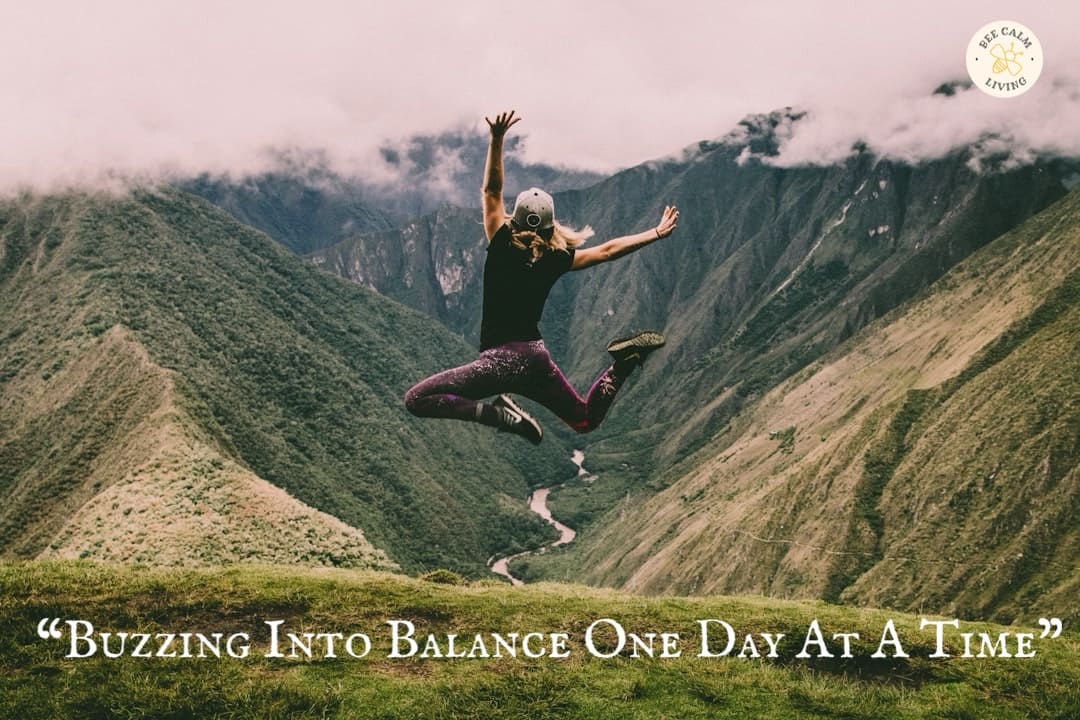 Bee Calm Living logo in the top right corner of an image of a woman jumping in front of green mountain view with “Buzzing into balance, one day at a time.” written in white across the bottom